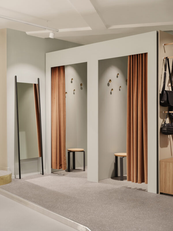 Dressing area with two changing booths, brown curtains, a mirror, and wooden stools in a modern retail space.