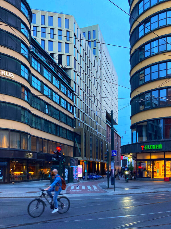 Evening view of Storgata street in Oslo, featuring modern buildings, a cyclist, and a 7-Eleven store.