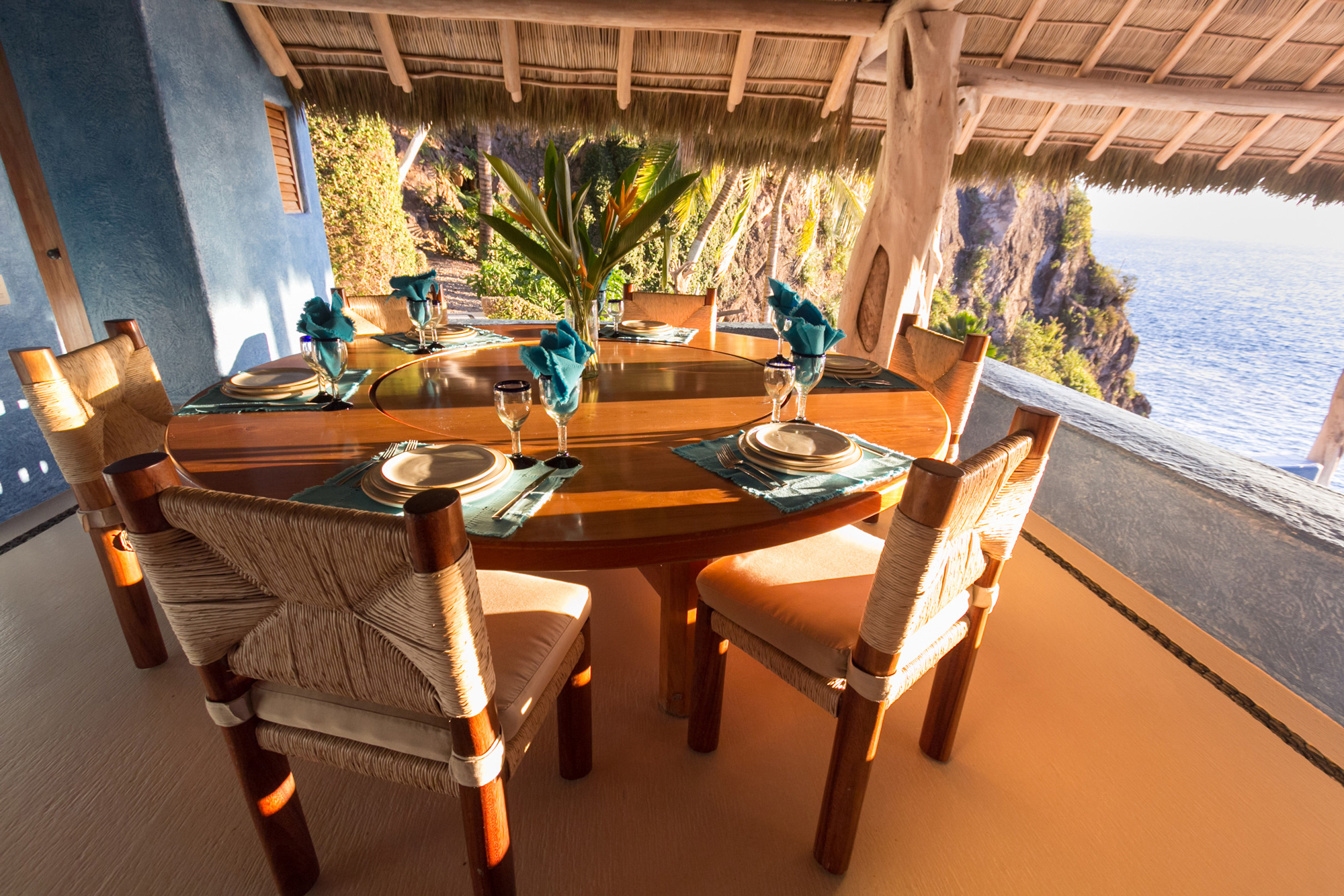 Elegant dining table set for six, adorned with blue napkins and tableware, overlooking a scenic ocean view.