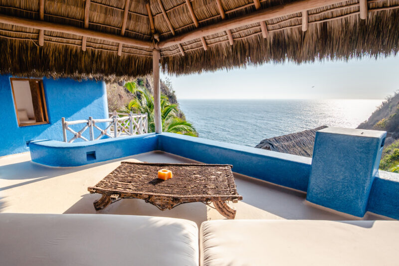Cozy terrace with a wooden table and an orange centerpiece, overlooking the ocean and lush greenery.