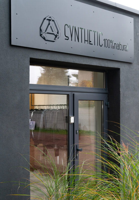 Entrance of a building featuring a sign that reads "SYNTHETIC 100% natural" above a glass door.