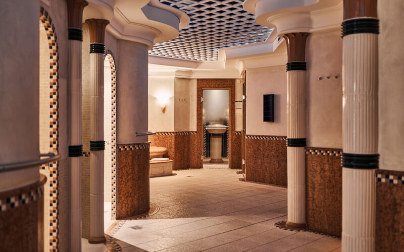 Elegant spa area with tiled columns, arches, and soft lighting, featuring a relaxation space and a sauna entrance.