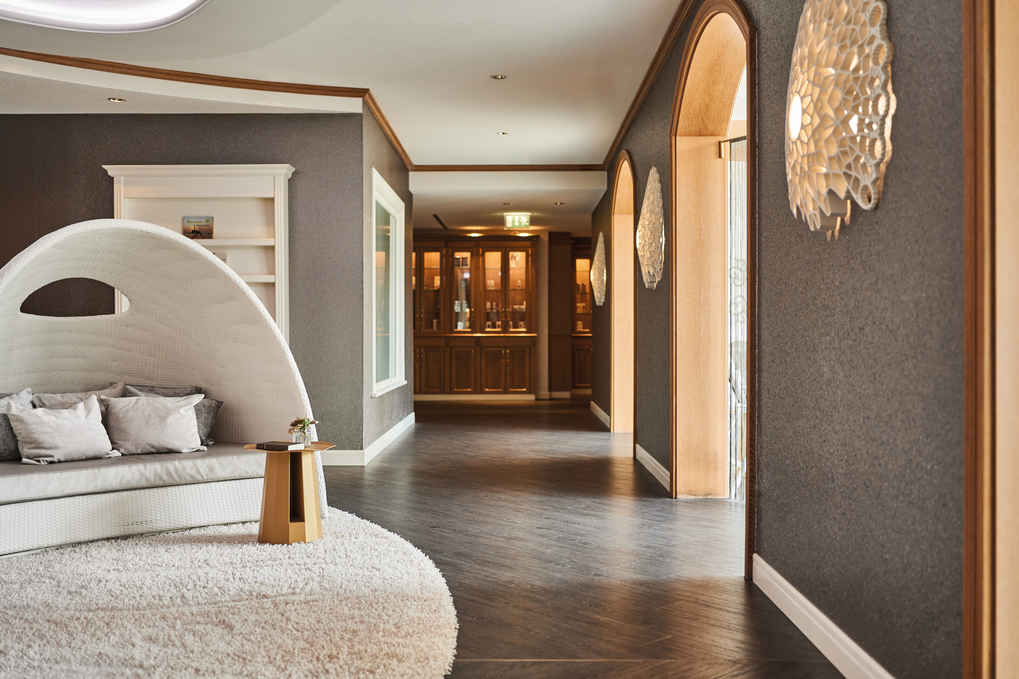 Sleek spa entrance featuring a white sofa, round table, and textured walls, with soft lighting and wooden accents.
