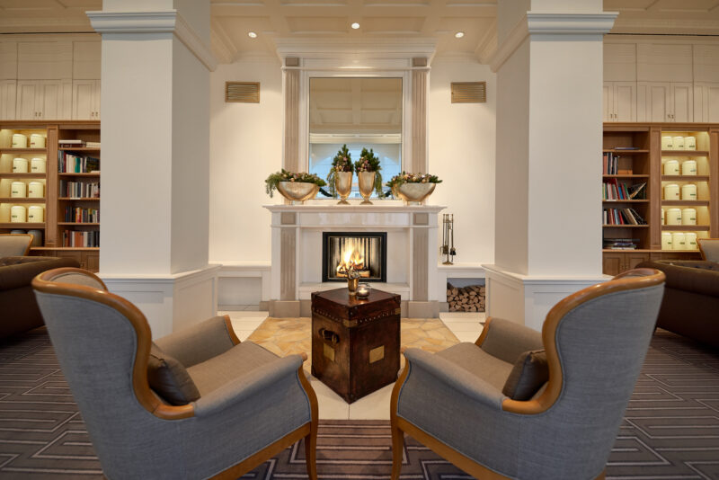 Cozy library scene at Kurhaus Binz featuring two armchairs, a fireplace, and bookshelves filled with books.
