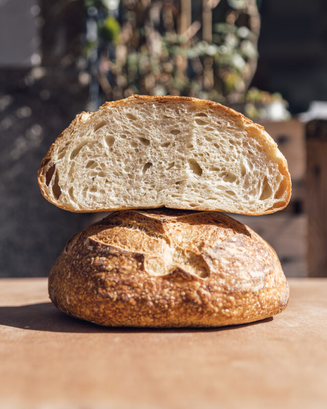 Sliced loaf of grano duro bread, showcasing its airy interior and crust, with a blurred background of greenery.