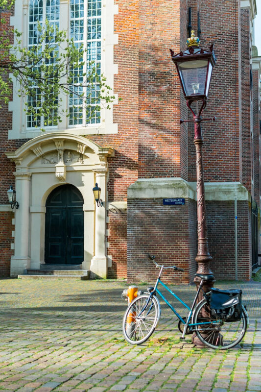 Bicycle leaning against a vintage lamppost in front of a brick building with large windows.