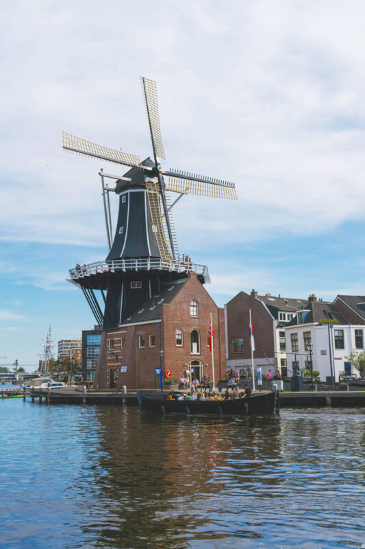 Traditional windmill beside a canal, with a boat carrying people in the foreground and a clear blue sky.