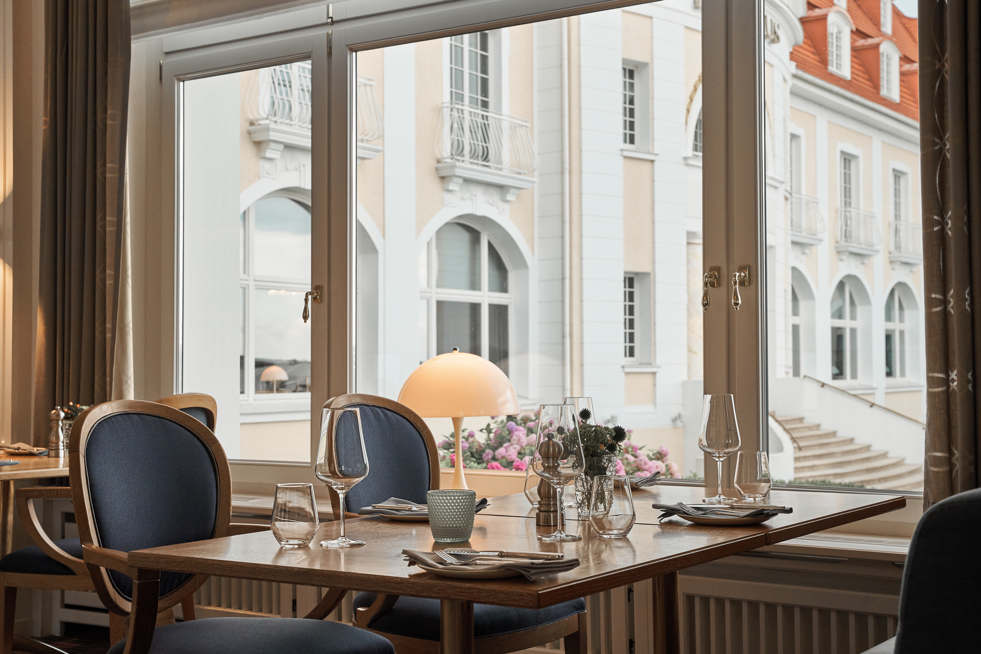 Frontal view of a four-person table set with glasses and a lamp, overlooking a terrace at Kurhaus Binz restaurant.