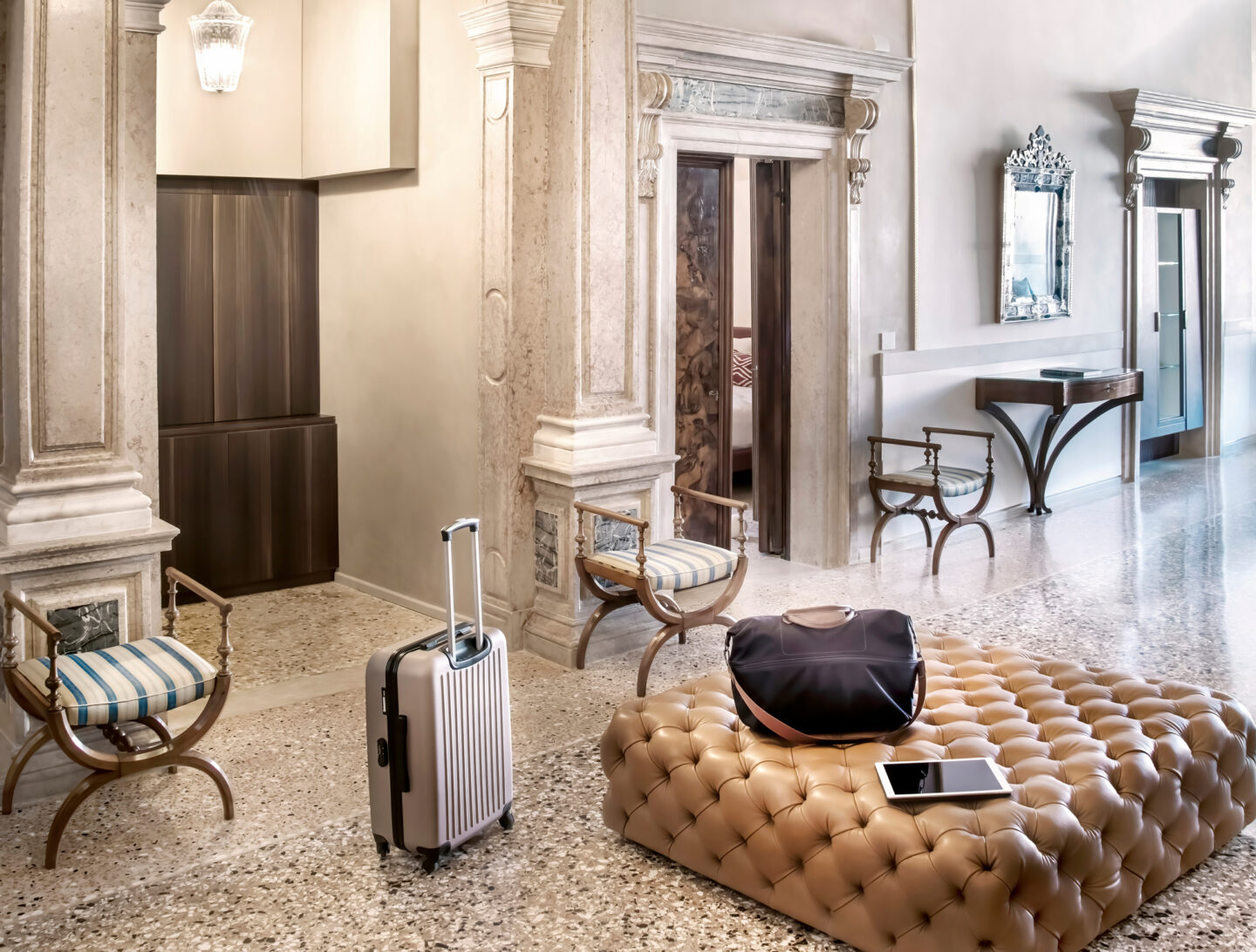 Elegant lobby of Palazzo Garzoni featuring a tufted ottoman, a suitcase, and stylish chairs on a polished floor.
