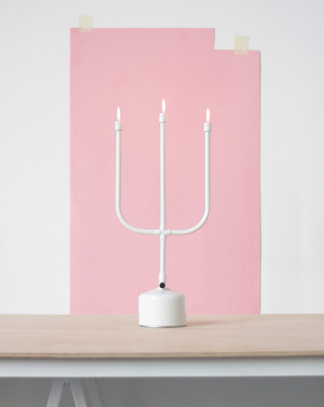 White three-armed candle holder with lit candles, set against a pink background on a wooden table.