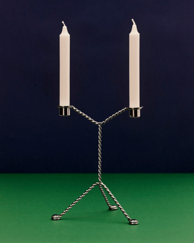 Candle holder with two white candles, made of twisted metal, set against a dark blue and green background.