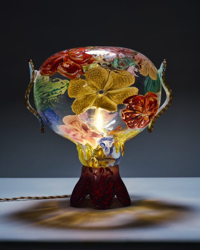 Colorful glass lamp with floral designs, featuring a bulb inside and a decorative base.