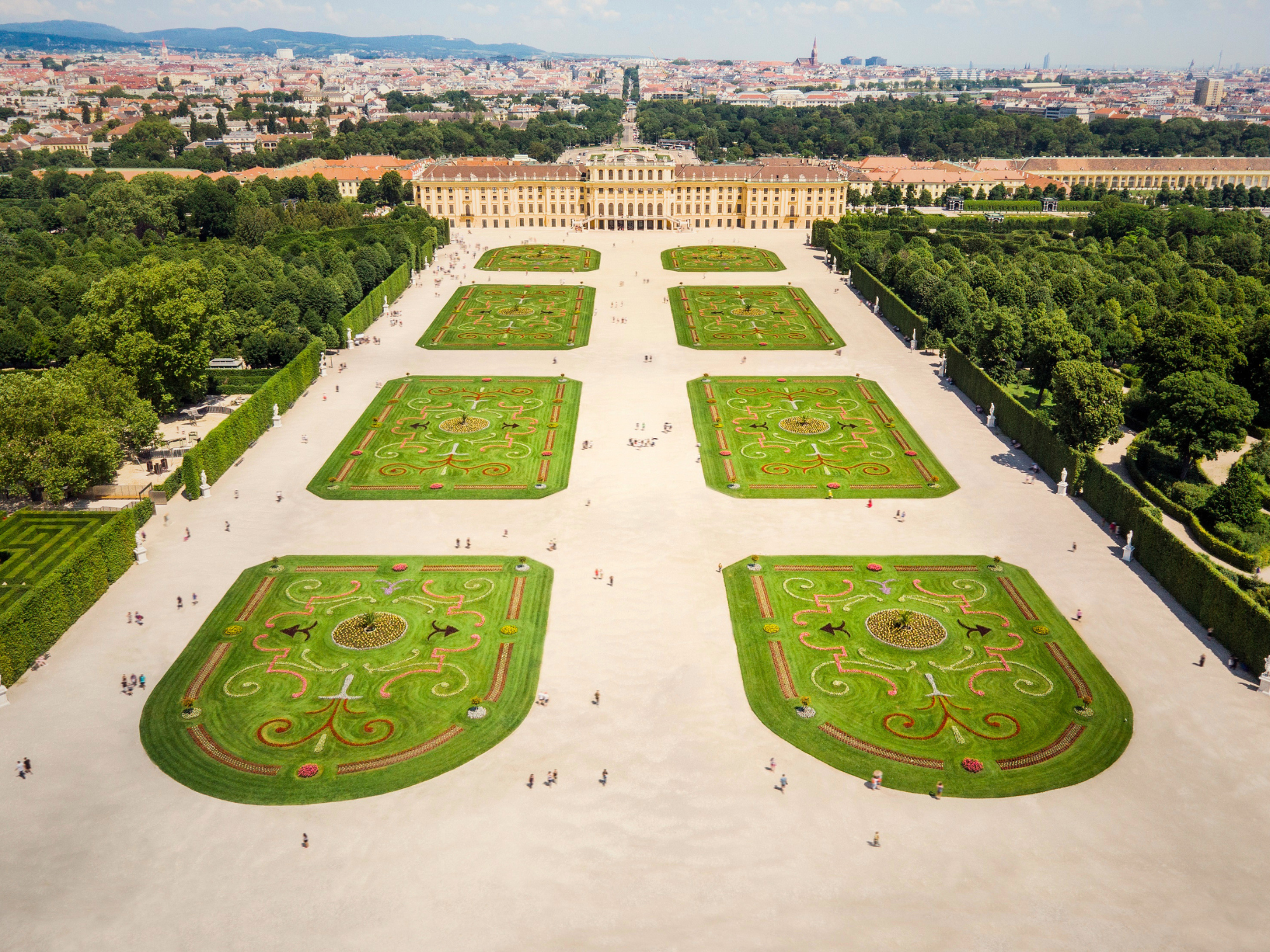 Aerial view of Schönbrunn Palace gardens in Vienna, featuring intricate floral designs and visitors walking along pathways.