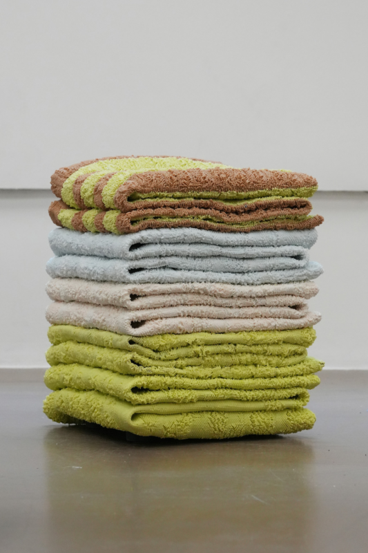 Stack of colorful towels in various shades, arranged neatly on a flat surface against a light background.
