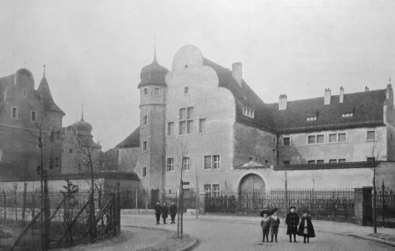 Historic prison building in Groß-Lichterfelde, featuring distinctive architecture and surrounding fence, with people in t...