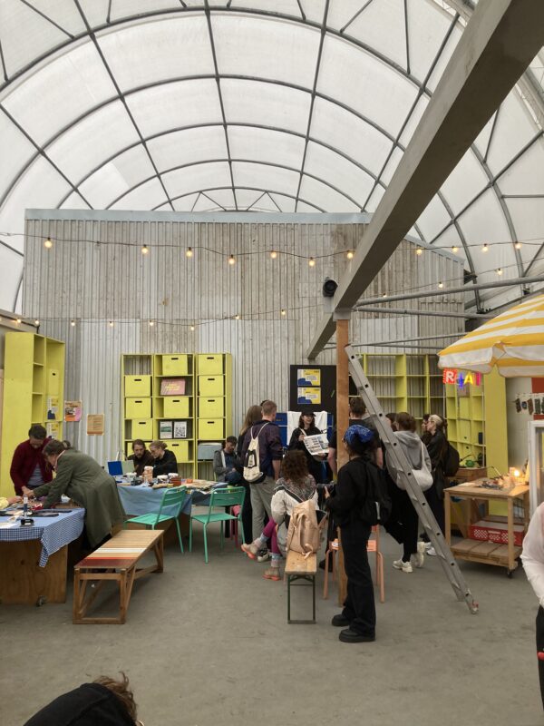 Interior of a vibrant community space with people engaged in activities, colorful furniture, and shelves filled with mater...