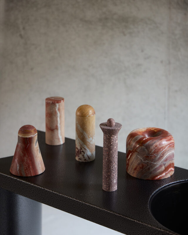 Five decorative stone objects in various shapes and colors displayed on a black surface against a textured gray background.