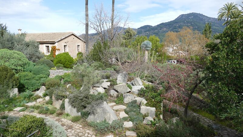 Botanical garden in Sóller with stone pathways, greenery, and mountains in the background.