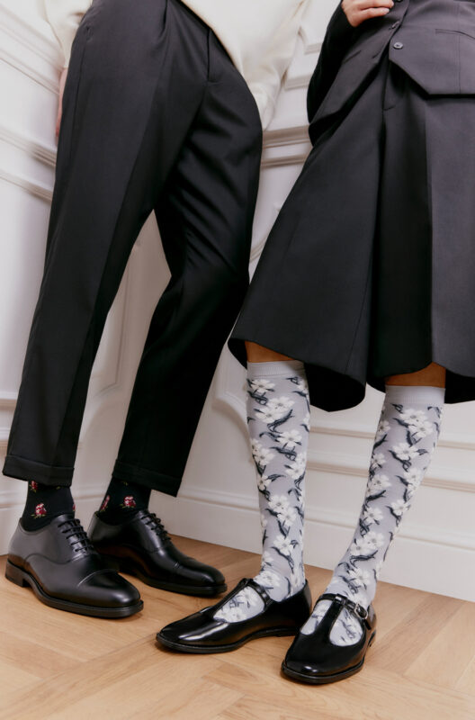 Two individuals wearing stylish outfits: one in black trousers and shoes, the other in a skirt and patterned knee-high socks.