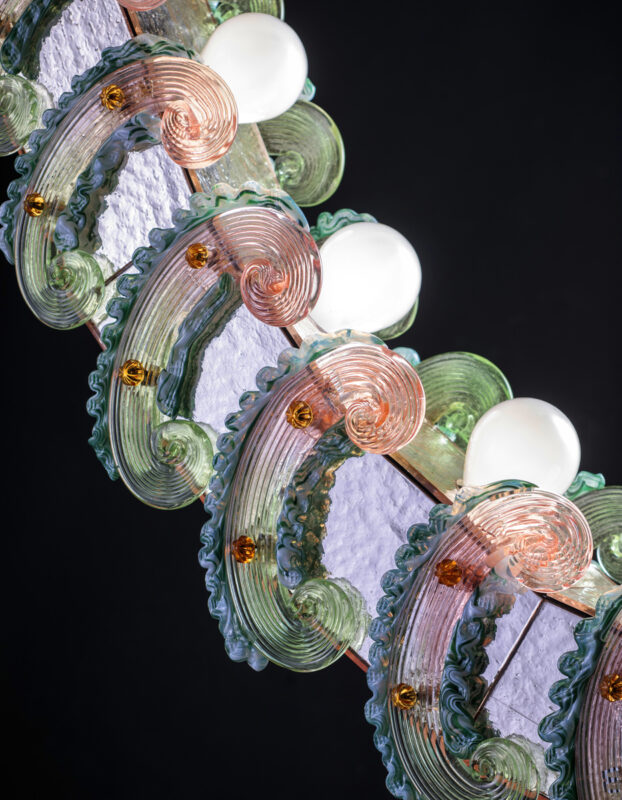Colorful glass light fixture with swirling mint green and pink designs, featuring round white bulbs, against a dark backgr...