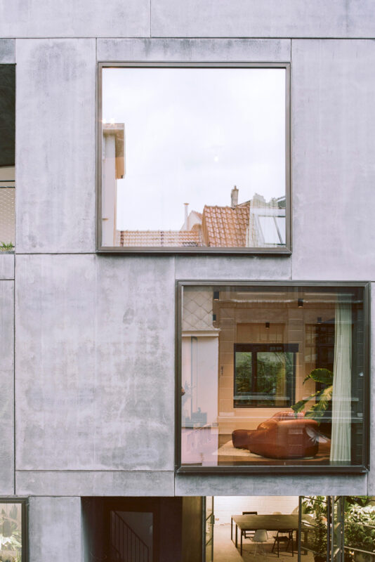 Modern building facade with large windows reflecting interior spaces and surrounding architecture.