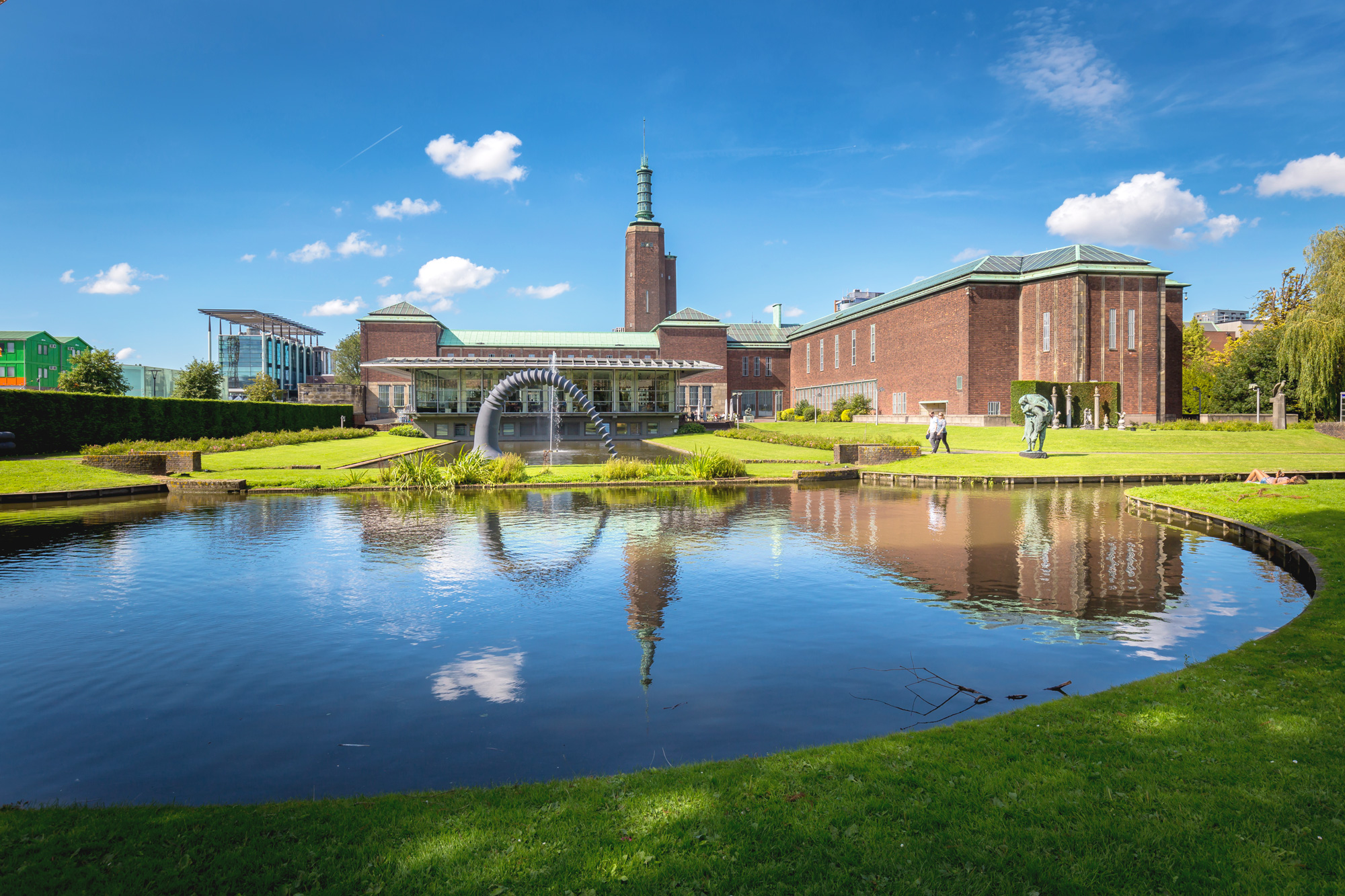 Museum Boijmans Van Beuningen with a reflecting pond, green lawns, and sculptures under a blue sky with clouds.