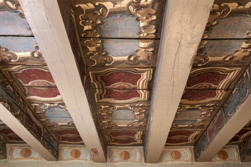 Ornate ceiling details with painted panels in red, blue, and gold, featuring wooden beams at Palazzo Garzoni.
