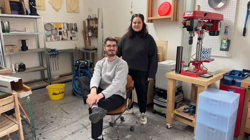 Jessie Derogy and Dorian Felgines pose in a workshop, surrounded by tools and equipment, with a relaxed atmosphere.