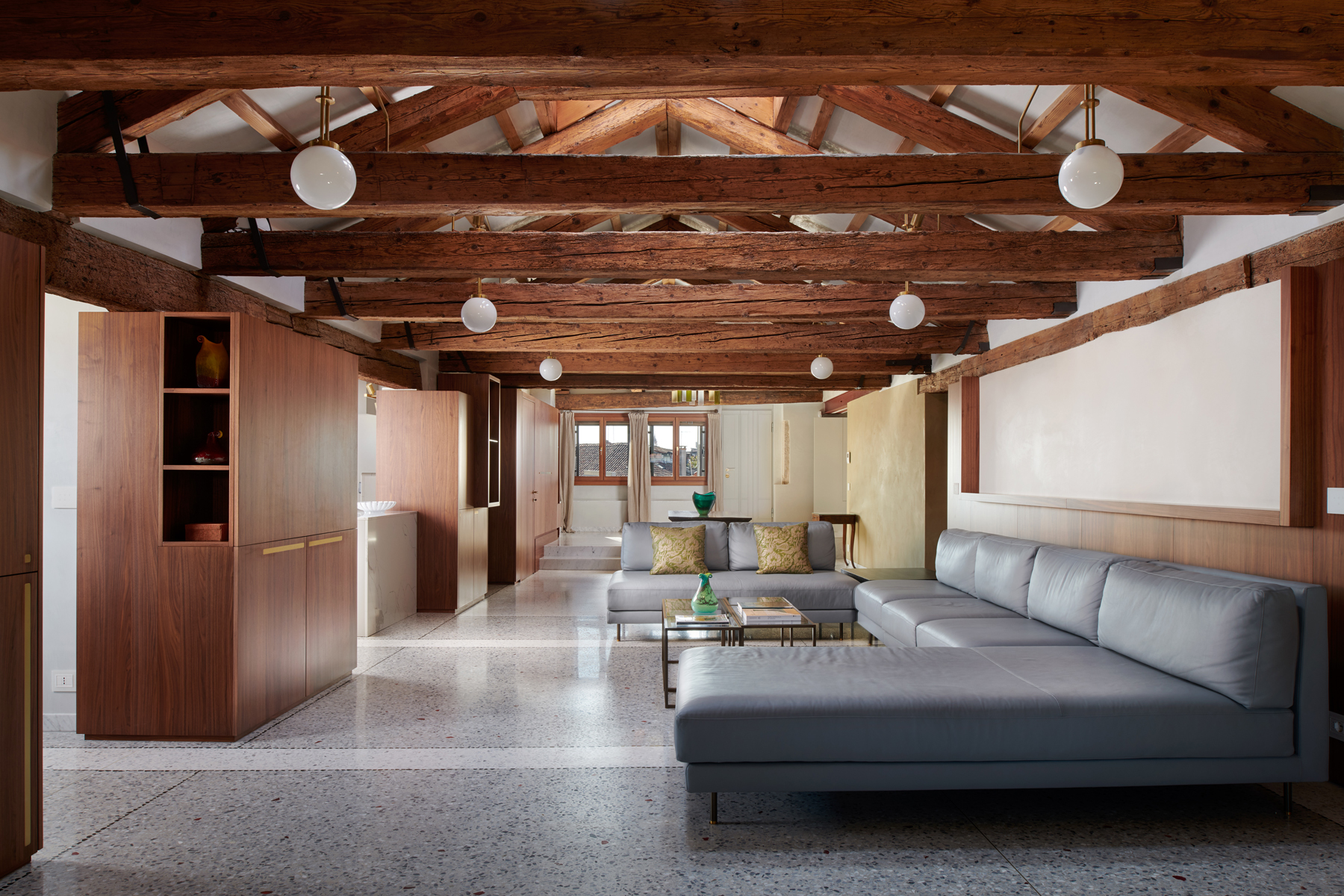 Modern lounge area in Palazzo Garzoni featuring a gray sectional sofa, wooden beams, and large windows.