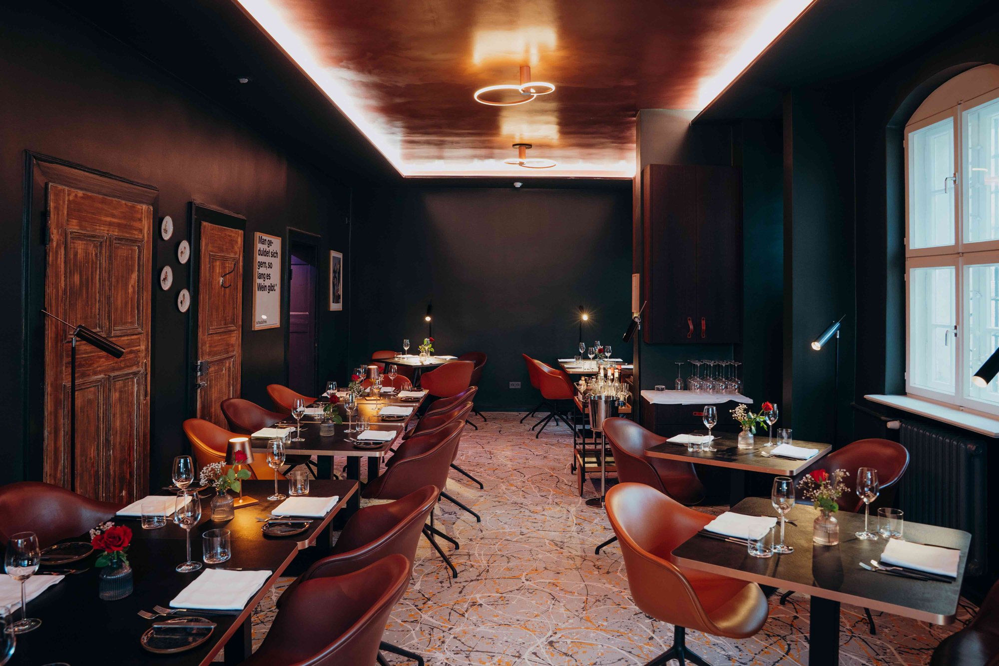 Elegant restaurant interior featuring dark walls, wooden doors, and stylish tables set with glassware and floral centerpie...