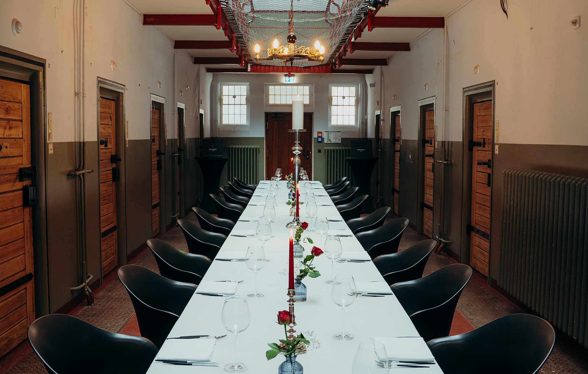 Long dining table set with candles and roses, flanked by prison cell doors in a historic building.