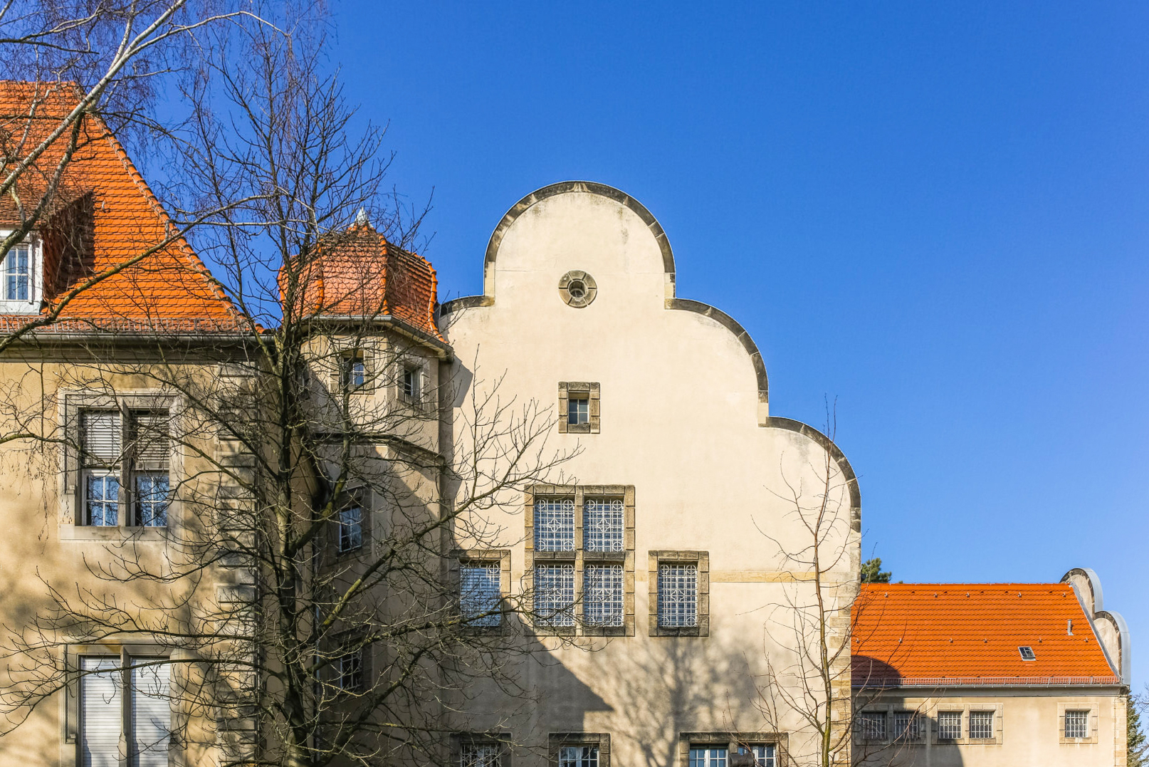 Historic building exterior with a distinctive gabled roof, surrounded by trees against a clear blue sky.