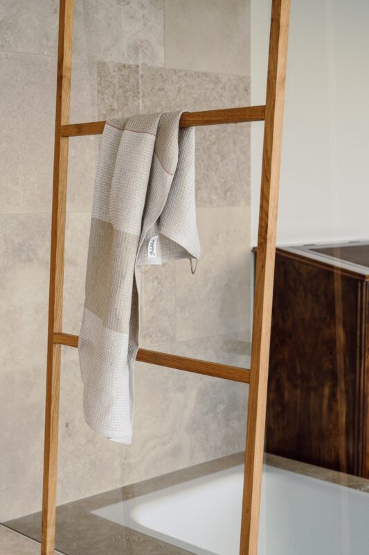 A beige and gray patterned towel hangs on a wooden ladder rack in a modern bathroom setting.