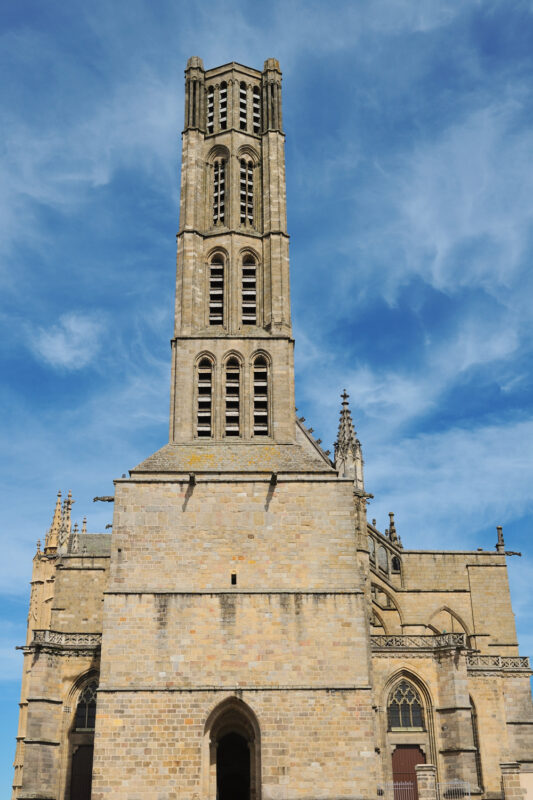 Facade of Limoges Cathedral, featuring a tall tower against a blue sky with scattered clouds.