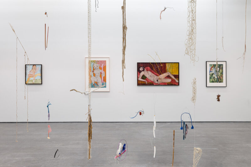 Art installation featuring hanging sculptures with framed artworks on the walls, displayed in a gallery setting.