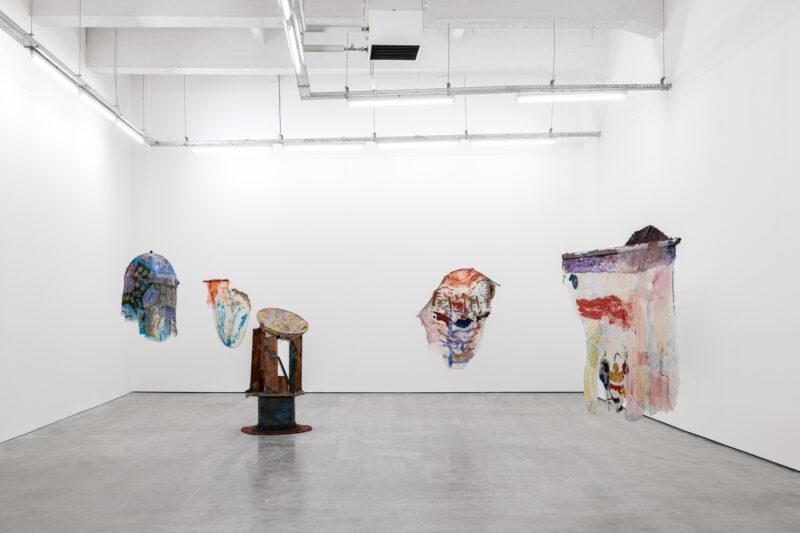 Art gallery interior featuring abstract artworks on white walls, with a central sculpture on a gray floor.