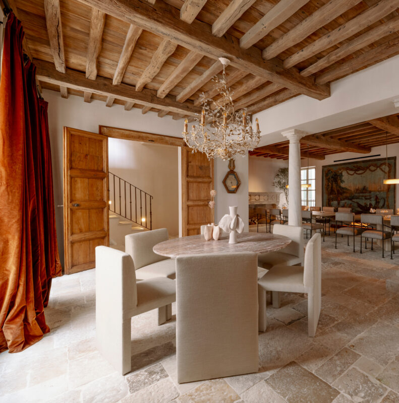 Elegant dining room featuring a round table with upholstered chairs, wooden beams, and a chandelier, with a warm color pal...