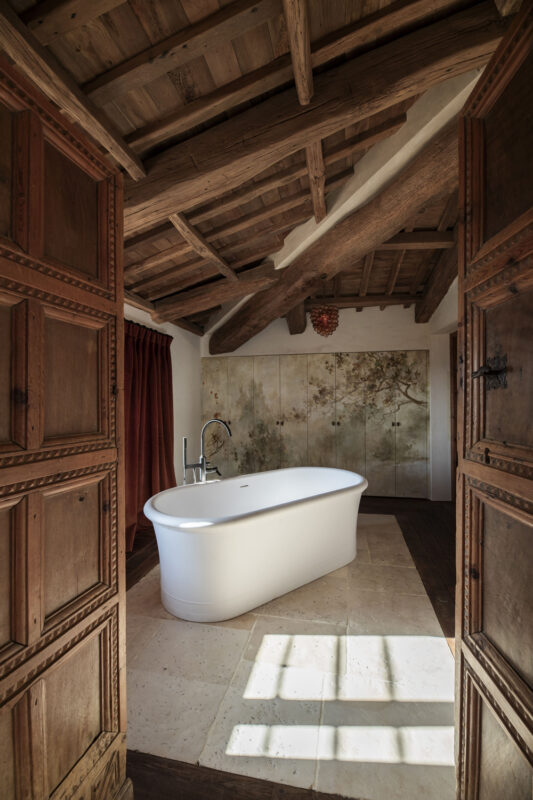Bright, modern bathroom featuring a freestanding white bathtub, wooden beams, and decorative wall panels.