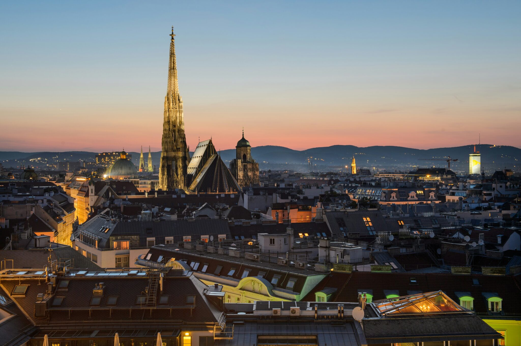 Vienna skyline at dusk, featuring St. Stephen's Cathedral and distant mountains under a colorful sunset.