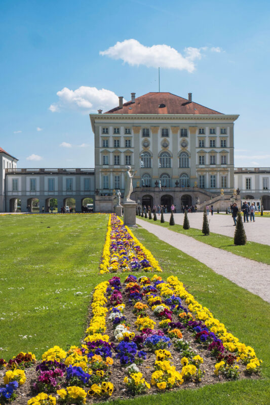 Baroque-style building with a manicured garden featuring colorful flower beds under a clear blue sky.