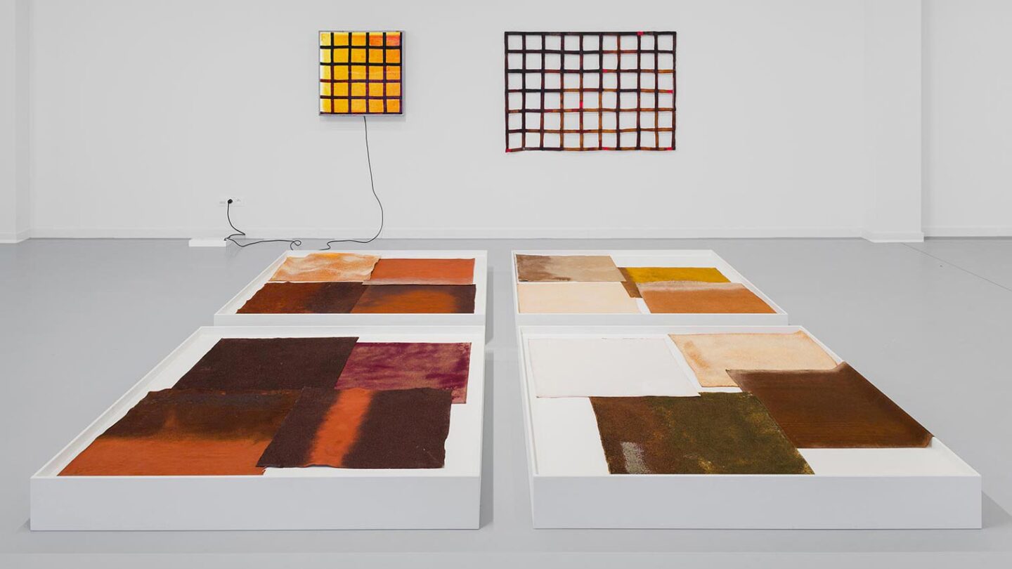 Abstract art installation featuring four large, rectangular color blocks on white platforms, with two grid-patterned artwo...