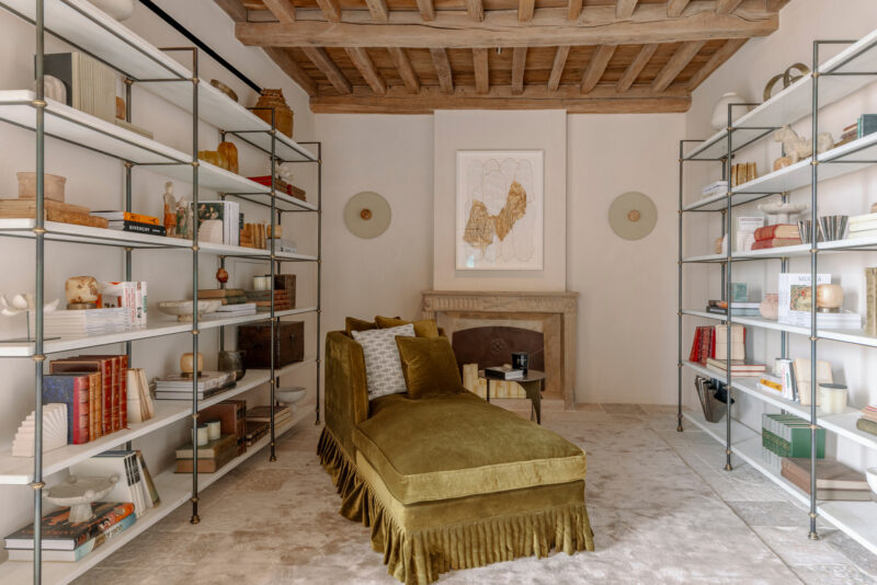 Cozy library with a green chaise lounge, bookshelves filled with books and decor, and a fireplace in a stylish interior.