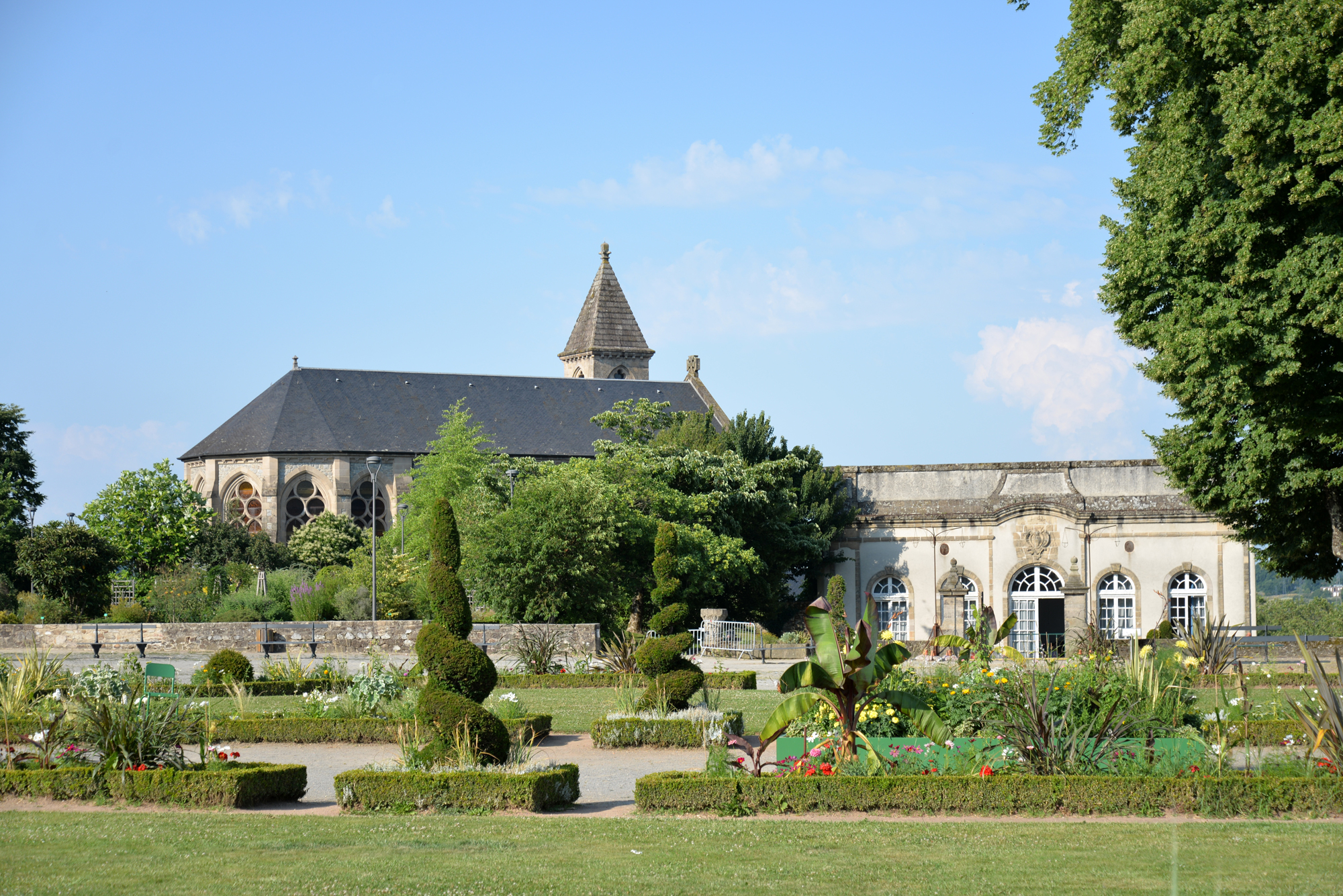 Historic building with a pointed roof and gardens featuring neatly trimmed hedges and colorful flowers in Limoges.