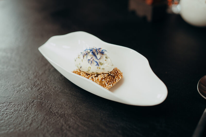 Delicate dessert served on a white plate, featuring a creamy topping garnished with blue flowers on a crispy base.
