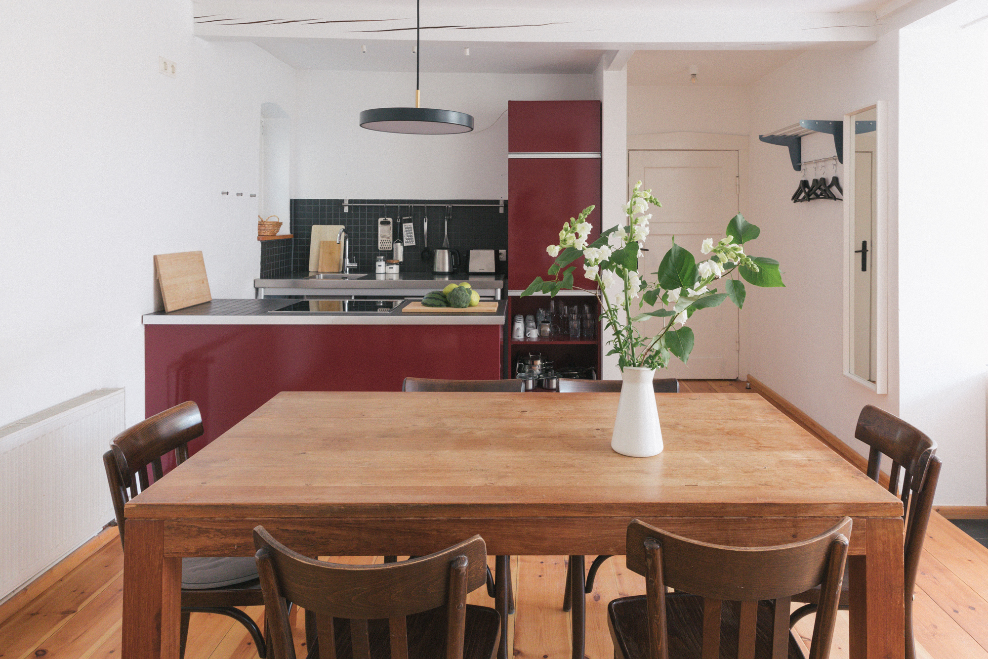 Modern kitchen and dining area featuring a wooden table, dark chairs, and a red kitchen unit with white walls.