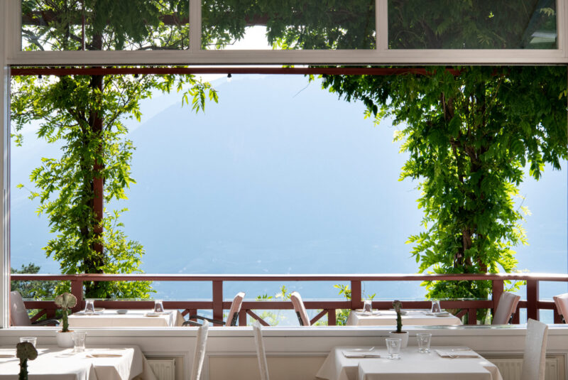View from the restaurant Orangerie at Castel Fragsburg, featuring tables and a scenic mountain backdrop.