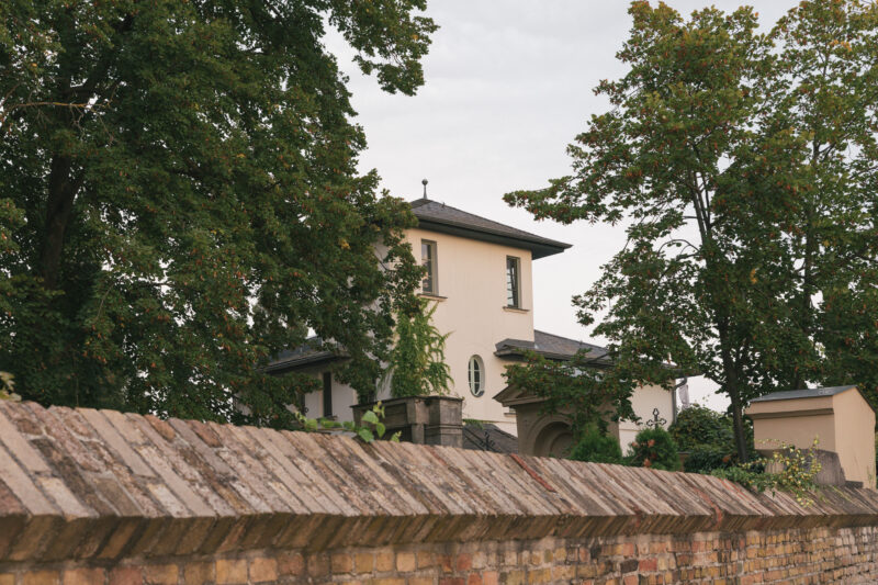 Bauhaus-style building partially obscured by trees, viewed behind a brick wall, in Werder.