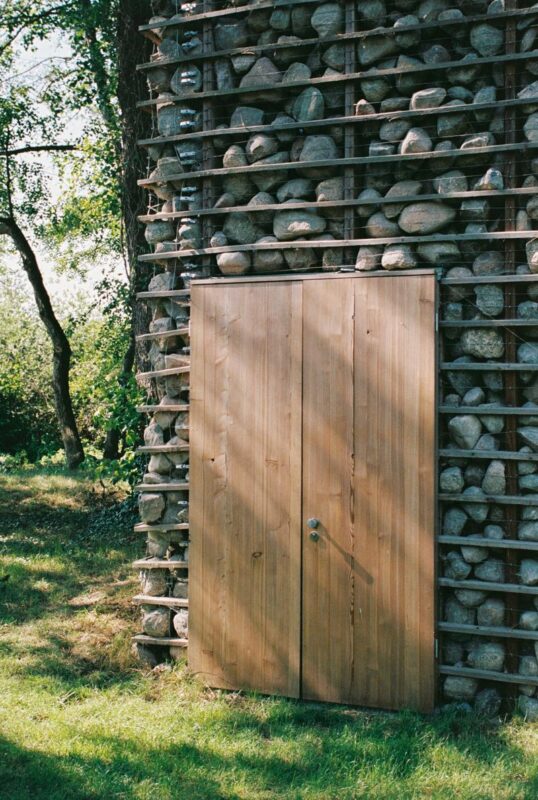 Wooden door set against a stone wall, surrounded by greenery, captured in a natural setting.