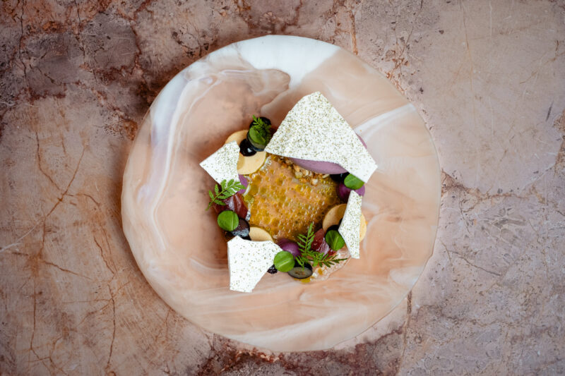 BBQ nectarine and blueberry meringue dessert garnished with herbs on a marbled plate.