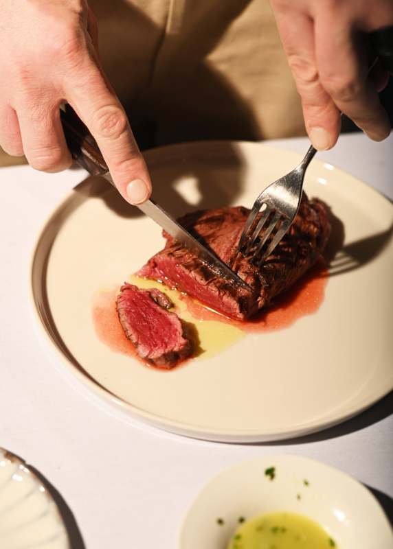 Juicy Chateaubriand steak being sliced on a plate, with a drizzle of sauce and a side of olive oil.
